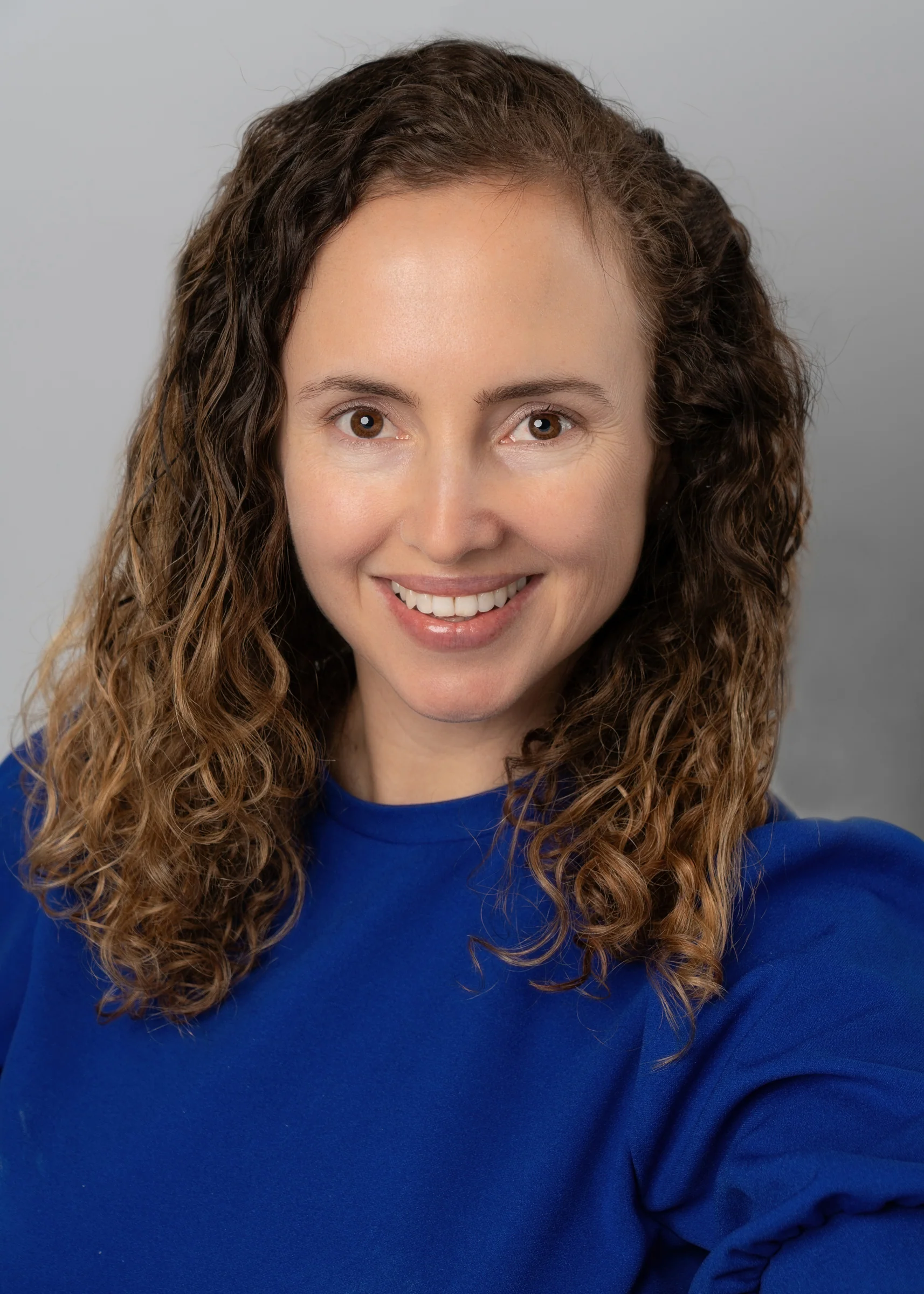 Portrait of a woman with brown hair on a flat gray background.